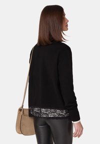 Zwarte trui met lange mouwen en kantdetails aan de onderkant, gecombineerd met nepleer broek en een tan crossbody tas.