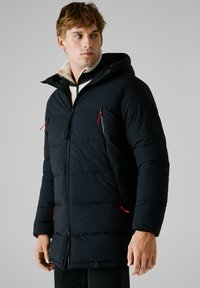 Chaqueta tipo puff en azul marino con capucha, que cuenta con bolsillos con cremallera y tiradores rojos. El forro interior es de una tela suave de contraste.