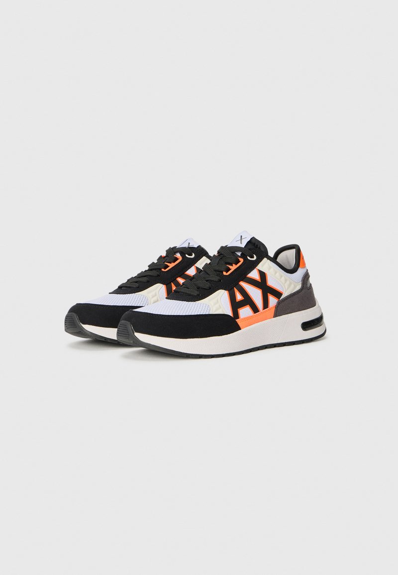 Zapatillas con una combinación de colores negro, blanco y naranja, con un upper texturizado, cuello acolchado y una suela blanca gruesa. Detalle del gran logo "AX".