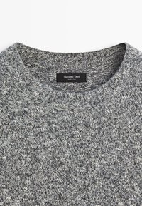 Maglione grigio a maglia con scollatura rotonda, realizzato in un tessuto testurizzato. Presenta leggere variazioni di colore e un'etichetta con la scritta "Massimo Dutti."