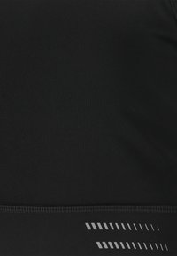 Musta urheilu-toppi, jossa on sileä pinta, ja joka presentaatihaa koristeellinen hopeanvärinen viivakuosi alareunassa sekä vahvistetut saumat.