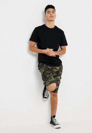 Svart T-skjorte med rund hals, camo-trykte shorts med rå kant, og svarte høye sneakers. Lett stoff, avslappet passform og shorts som går til kneet.