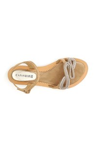 Beige-suede sandaalit, joissa on kaareva hopeinen helmikoriste. Säädettävä nilkkahihna ja sileä, ruskea pohja, jossa on ommellut reunat. Tasapohja.