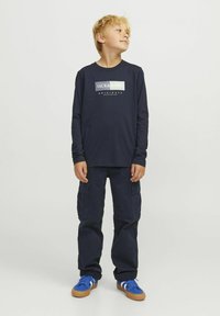 Šalavnavimo mėlyna ilgomis rankovėmis marškiniai su "JACK & JONES" logotipu, derinami su mėlynomis cargo kelnėmis ir mėlynais sportbačiais su baltais akcentais. Pagaminti iš medvilnės, laisvo kirpimo.