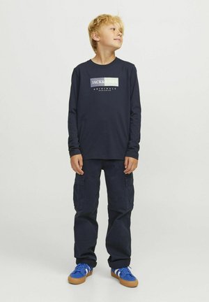 Camisa de manga larga color navy con el logotipo "JACK & JONES", combinada con pantalones cargo navy y zapatillas azules con acentos blancos. Material de algodón, corte casual.