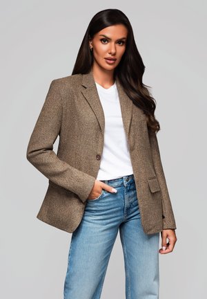 Blazer en tweed marron avec une fermeture à un bouton, revers crantés et poches avant, associé à un t-shirt blanc et un jean en denim bleu.