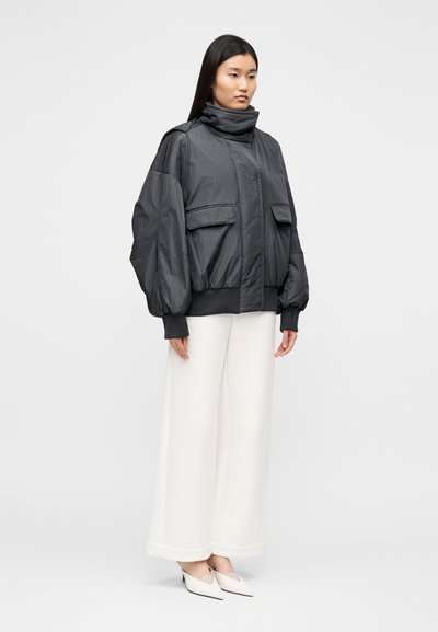 Juoda, per dydį didelė pūkinė striukė su aukštu apykakliu, dviem priekinėmis kišenėmis ir elastiniais rankogaliais. Dėvima ant baltų plačių kelnių ir baltų aukštakulnių.