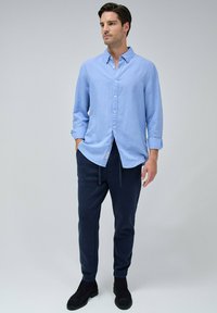 Camisa de botones azul claro de lino, combinada con pantalones jogger azul marino oscuros y zapatos negros. La camisa tiene un cuello casual y las mangas arremangadas.