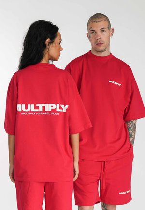 Rode oversized t-shirts met het "MULTIPLY" logo in het wit op de voor- en achterkant, gecombineerd met bijpassende rode shorts. Soepele stof en een relaxte pasvorm.