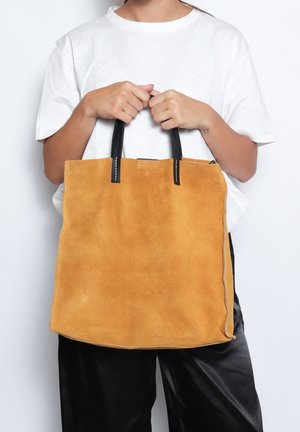 Borsa tote in suede gialla senape con manici in pelle nera e cuciture bianche. Design rettangolare semplice con superficie testurizzata.