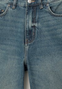 Blue denim jeans with a faded wash, featuring copper stitching, a metal button, and two front pockets. The fabric has a smooth texture.