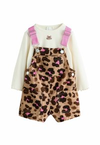 Braune Corduroy-Latzhosen mit Leopardenmuster und pinken Akzenten, kombiniert mit einem weißen Langarmshirt mit einem Katzenmotiv.
