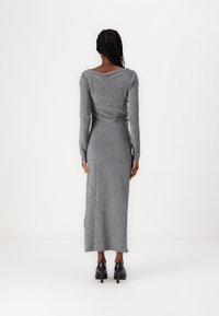 Abito lungo a maniche, in tessuto argentato, dalla linea aderente, con scollatura a barca sulla schiena e spacco laterale. Scarpe nere con tacco alto completano il look.