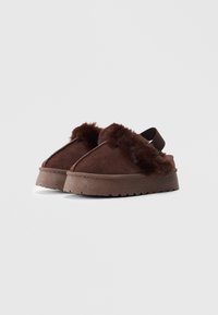 Pantofole marroni senza lacci con suole in gomma spesse e fodera in pelliccia sintetica marrone scuro attorno all'apertura e cinturino elastico sul tallone per una vestibilità sicura.