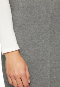 Tissu gris en mélange de laine avec une texture douce, présentant un design ajusté. Une chemise blanche à manches longues dépasse en dessous.