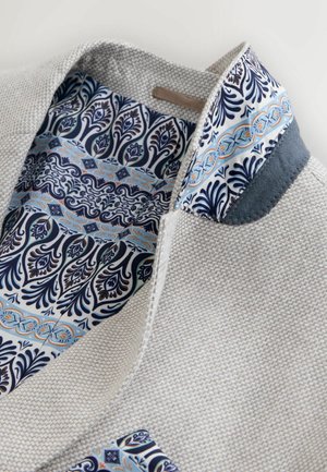 Grau strukturierte Jacke mit einem gemusterten blauen Innenfutter, das Wirbel- und Blumendesigns zeigt. Auffällige Kragenapplikationen aus marineblauem Material.