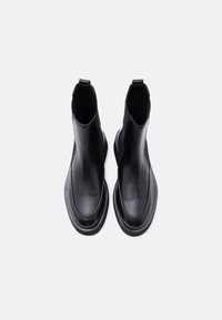 Paire de bottines Chelsea en cuir noir avec bouts arrondis et semelles épaisses, vues de dessus sur un fond blanc uni.