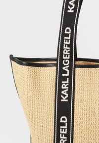 Gewebte Strohtasche mit schwarzem Lederbesatz, ausgestattet mit einem breiten Trageriemen mit "KARL LAGERFELD" in weißem Text und einer strukturierten Form.
