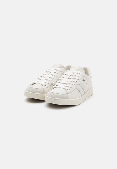 Hvide lædersneakers med grå ruskindsdetaljer, flade snørebånd og en struktureret gummisål. Har et diskret logo på siden.