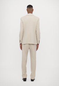 Completo beige chiaro con una vestibilità su misura, caratterizzato da una giacca monopetto e pantaloni dritti, realizzato in tessuto liscio.