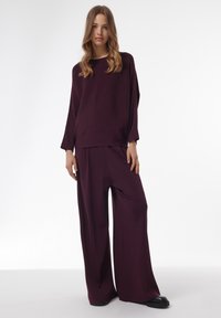 Pull en tricot bourgogne avec des manches larges associé à un pantalon ample assorti, doté d'une texture lisse et d'une silhouette décontractée.
