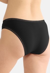 Sort bomuldstrusser med bølget blonderkant langs linningen og benåbningerne, der fremviser en glat tekstur og klassisk design.