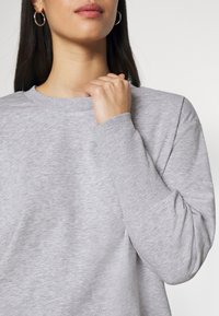 Felpa grigia chiara con collo a giro, polsini a costine e vestibilità rilassata. Tessuto liscio e design minimalista.