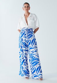 Chemise blanche à manches courtes avec une poche, assortie à un pantalon large avec un motif de feuilles bleues sur fond blanc. Texture de tissu lisse.