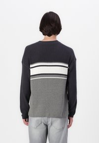 Knit sweater featuring a ribbed texture, dark gray and light gray body with horizontal white and navy stripes across the shoulders.