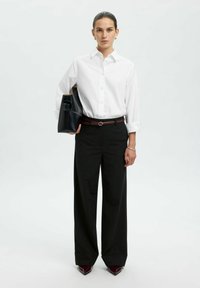 Witte knopshirt met opgerolde mouwen, gecombineerd met hoge zwarte wijdgesneden broeken en een zwarte handtas. Donkerrode puntige hakken.