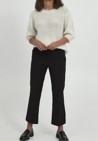 Weißer Strickpullover mit Rundhalsausschnitt und kurzen Ärmeln, kombiniert mit hochtaillierten schwarzen Hosen und schwarzen Slippern. Glatte Textur, lockere Passform.