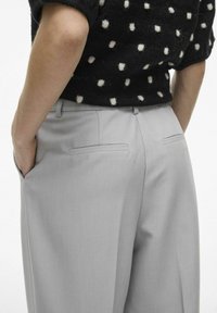 Pantalons ajustés gris clair avec une texture lisse, dotés de deux poches arrière et d'un design à l'avant plat, portés avec un haut noir à pois.