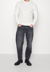 Pull blanc texturé avec des poignets côtelés, associé à un jean droit gris foncé et des bottes chelsea noires. Détail de logo subtil sur le pull.