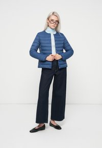 Modrá prešívaná puffová bunda s horizontálnymi prúžkami, cvokovými gombíkmi a golierom. Nosená na svetlomodrom roláku a kombinovaná s tmavými džínami.