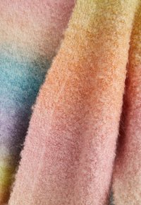 Gros plan d'un tissu doux et texturé avec un dégradé de couleurs pastel incluant du rose, orange, jaune, bleu et violet.