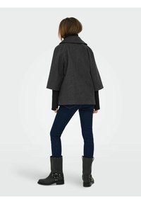 Szary, teksturowany płaszcz z szerokim kołnierzem i krótkimi rękawami, zestawiony z dopasowanymi ciemnymi dżinsami i czarnymi botkami za kostkę.