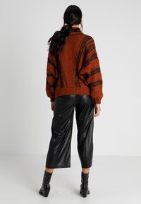 Suéter de color óxido con patrón a rayas, textura de punto grueso y cuello alto; combinado con pantalones de imitación piel negros de pierna ancha y botas de tobillo.