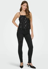 Czarny top na cienkich ramiączkach z cekinami; do tego czarne, postrzępione obcisłe jeansy oraz mule na szpic. Proste srebrne dodatki w postaci biżuterii.