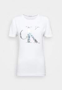 Camiseta de algodón blanca con cuello redondo y mangas cortas, que presenta un logo reflectante "CK" en tonos plateados y azules en la parte delantera.