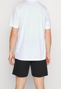 T-shirt de sport blanc à manches courtes, associé à un short noir. Le t-shirt présente un design simple et un tissu lisse et léger.