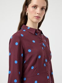 Weinrotes Kleid mit leuchtend blauen Punkten, durchgeknöpfter Vorderseite und Kragen. Glatter Stoff, lange Ärmel und reguläre Passform.