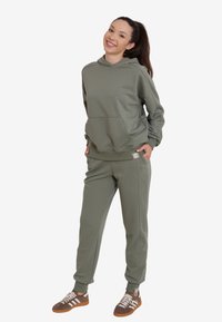 Khaki dwuczęściowy dres z bluzą z kapturem, przednią kieszenią i dopasowanymi spodniami, w połączeniu z brązowymi i białymi sneakersami.