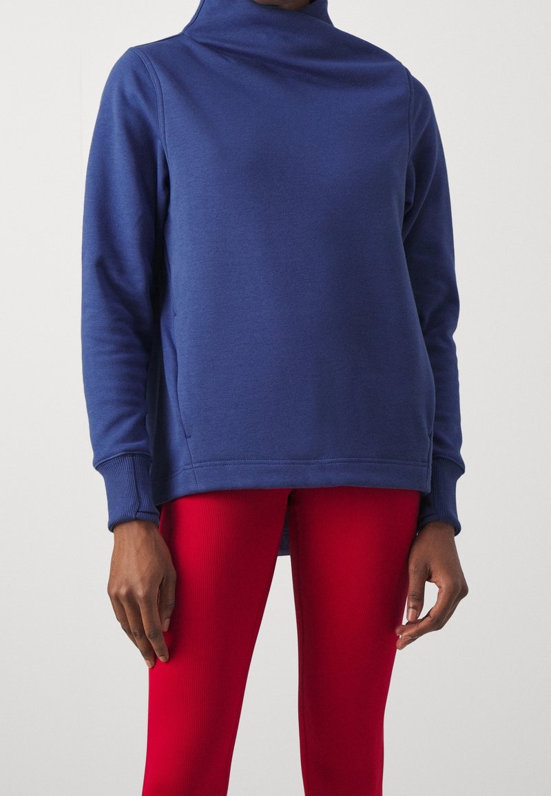 Sweatshirt en polaire bleu marine avec un col montant, des poignets côtelés et des coutures latérales, associé à des leggings rouges côtelés.