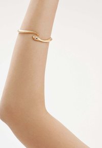 Pulsera de mano en forma de serpiente dorada con un diseño texturizado, que presenta un detalle brillante, llevada en un brazo desnudo sobre un fondo neutro.