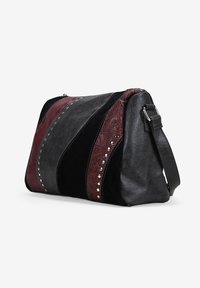 Borsa in pelle nera e borgogna con embossing floreale, borchie metalliche, strisce diagonali e una tracolla regolabile su sfondo neutro.