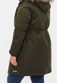 Abrigo parka verde oliva con capucha de pelo sintético, cintura ceñida y una textura suave; presenta puños negros y un acento blanco cerca del dobladillo.