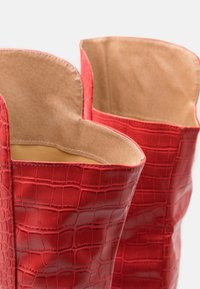 Detailní záb�ěr na červené kožené boty s krokodýlím vzorem, se světle béžovým vnitřním podšívkou a vlnitými okraji v horní části.