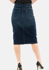 Mørk denim blyantskirt med en midt-længde, to baglommer og synlige syninger. Kombinationen med sorte højhælede sko.
