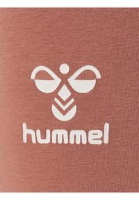 Conception de logo en blanc sur un tissu texturé de rose poussiéreux. Comprend une abeille stylisée avec des ailes courbées au-dessus du nom de la marque "hummel."