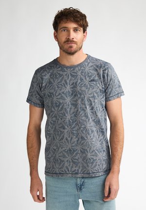 T-shirt à motifs bleus avec un design de feuille, fabriqué dans un tissu doux avec un col rond. Associé à un jean en denim bleu clair.